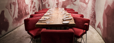 Langer Holztisch mit roten Samtsesseln in elegantem, gedämpft beleuchtetem Raum.