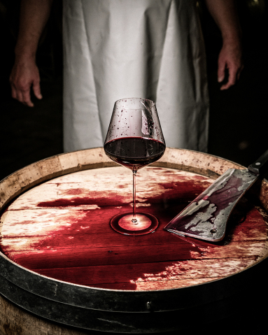 Weinglas und Hackmesser auf Fass mit roter Flüssigkeit, düstere Beleuchtung.