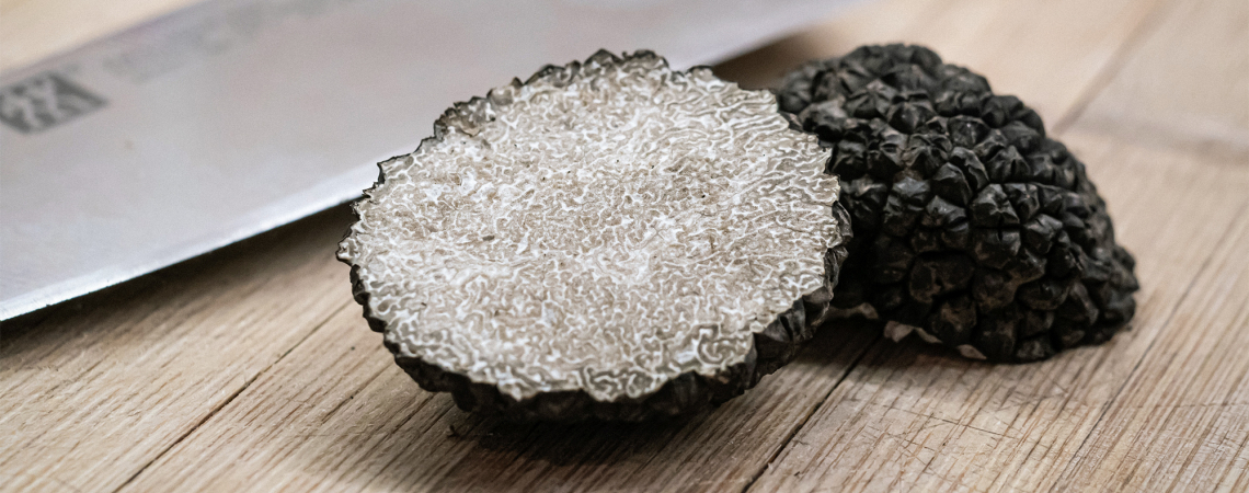 Grobe schwarze Trüffel auf Holzbrett neben einem Metallmesser.
