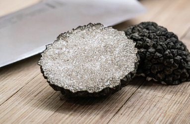 Grobe schwarze Trüffel auf Holzbrett neben einem Metallmesser.