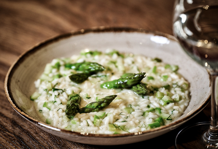 Cremiges Risotto mit grünem Spargel in einer rustikalen Schale, Holztisch.
