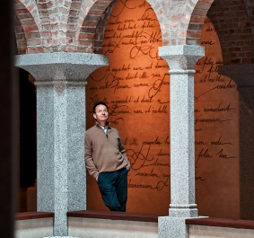 Person in historischem Gebäudegang mit Ziegelbögen und Steinsäulen.