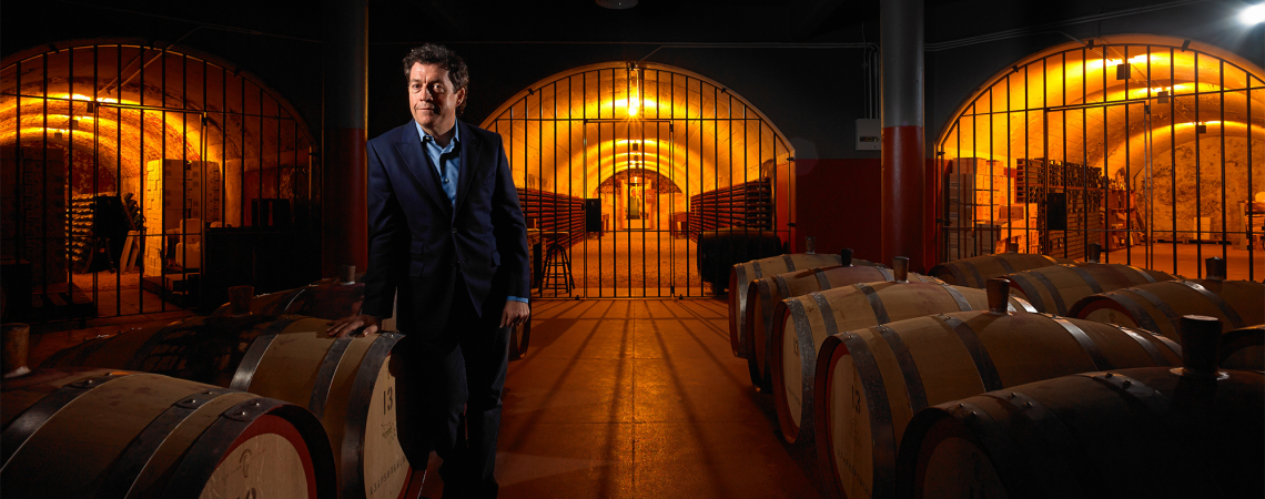 Ein Mann in einem Weinkeller mit Fässern und warmem Licht.