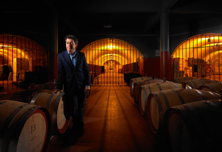 Ein Mann in einem Weinkeller mit Fässern und warmem Licht.