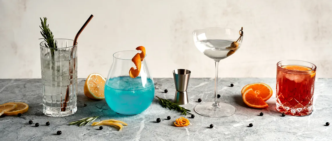 Vier bunte Cocktails mit Garnitur auf grauem Marmorhintergrund.