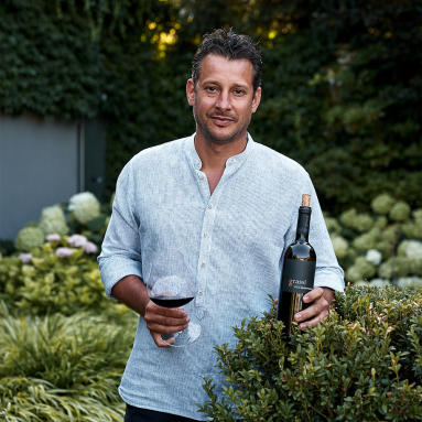 Mann im blauen Hemd mit Weinglas und Weinflasche im Garten.