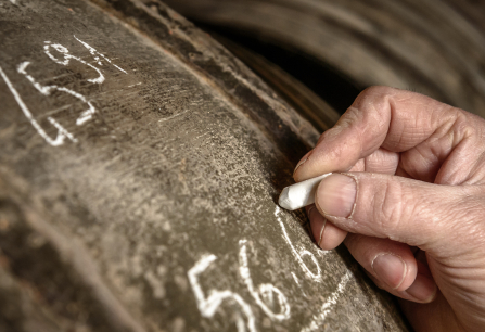 Hand schreibt mit Kreide auf eine alte, hölzerne Weinfassoberfläche.