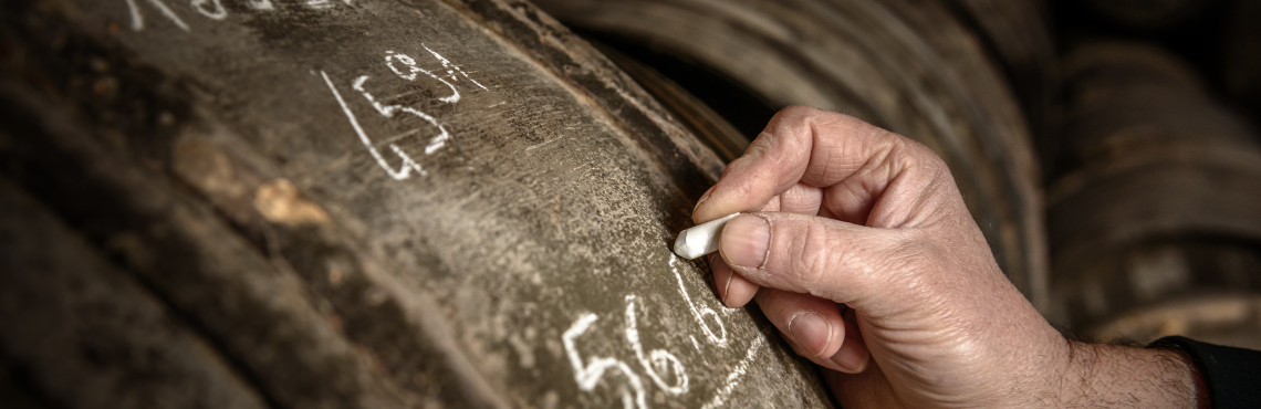 Hand schreibt mit Kreide auf eine alte, hölzerne Weinfassoberfläche.