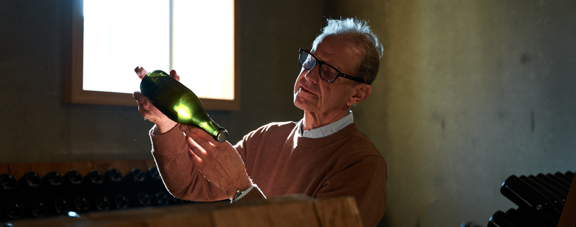 Mann inspiziert Weinflasche im von natürlichem Licht beleuchteten Raum.