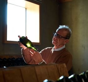 Mann inspiziert Weinflasche im von natürlichem Licht beleuchteten Raum.