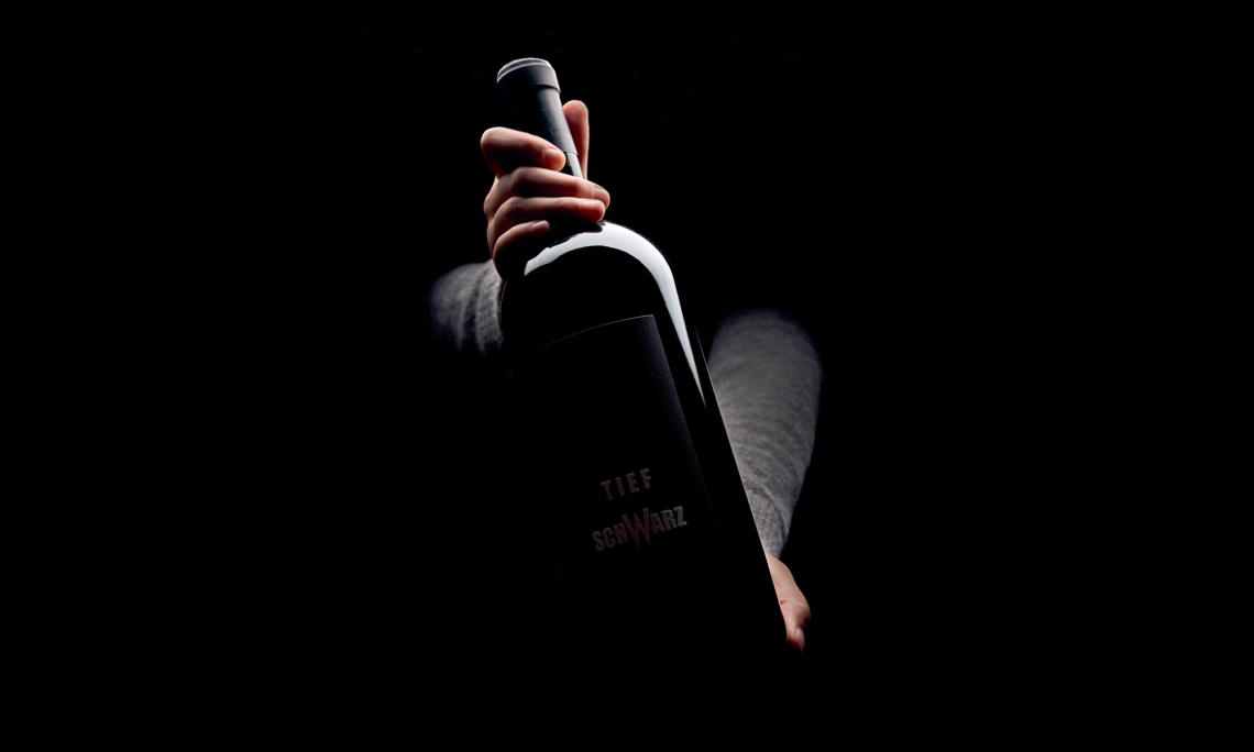 Große Weinflasche in Hand vor dunklem Hintergrund.