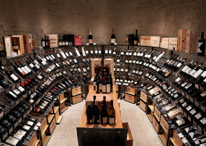 Weinkeller mit gebogenen Regalen voller Weinflaschen und Holzkisten.