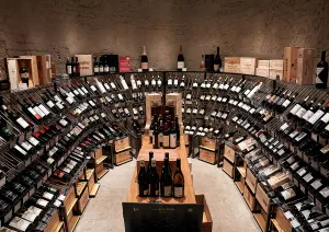 Weinkeller mit gebogenen Regalen voller Weinflaschen und Holzkisten.