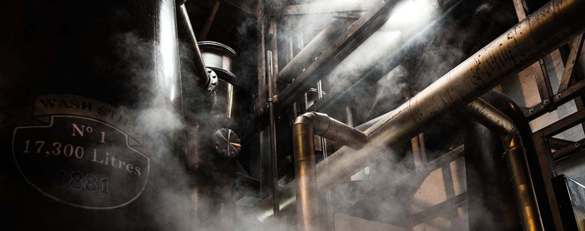 Dampfende industrielle Anlage mit sichtbaren Rohren und warmem Licht von oben.