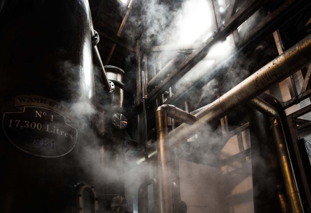 Dampfende industrielle Anlage mit sichtbaren Rohren und warmem Licht von oben.