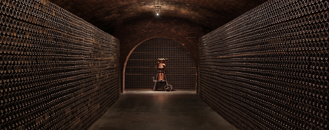 Gewölbekeller mit gestapelten Weinflaschen an den Wänden.