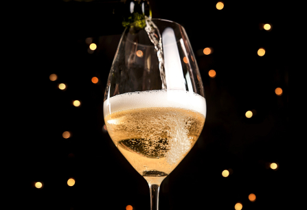 Sektglas mit sprudelndem Getränk, im Hintergrund warme Lichtakzente.