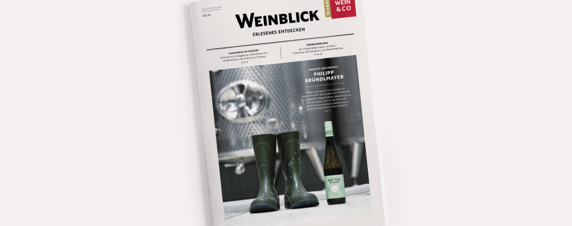 Weißes Magazin mit Bild von grünen Gummistiefeln und Weinflasche im Industriebereich.