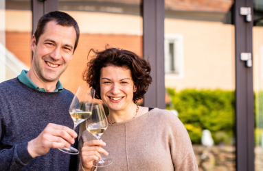 Zwei lächelnde Personen stoßen mit Sektgläsern im Freien an.