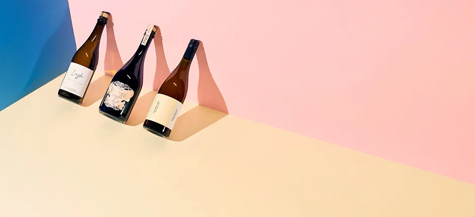 Drei Weinflaschen auf pastellfarbenem Hintergrund mit Schattenwirkung.