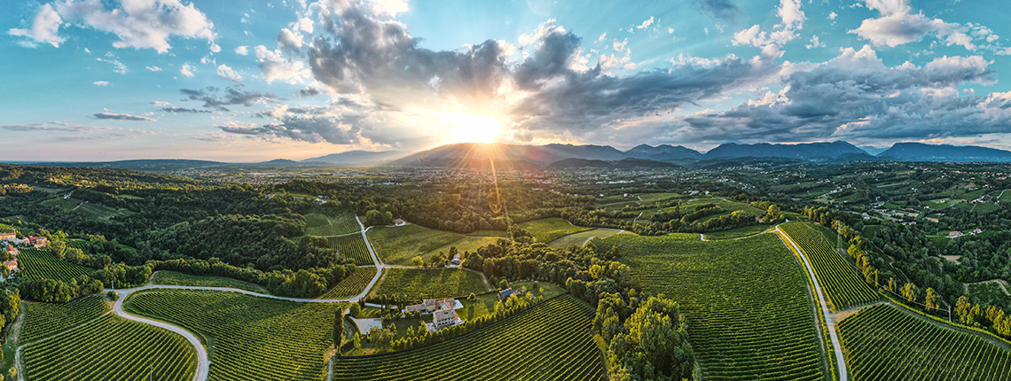 Landschaftspanorama mit Weinbergen, Straßen und einem dramatischen Sonnenuntergang am Horizont.