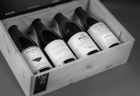 Vier Flaschen Wein in einer offenen Holzkiste, kunstvoll angeordnet.