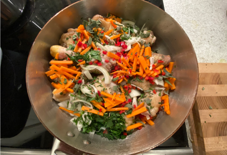 Kupferpfanne mit Hähnchenkeulen, Karottenstreifen, Zwiebeln und Kräutern auf Herd.