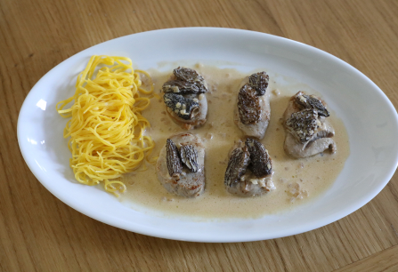 Medallions mit Pilzen in heller Soße, serviert mit gelben Nudeln auf weißem Teller.