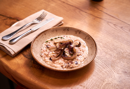 Cremiges Risotto mit gegrillten Zwiebeln auf rustikalem Holztisch serviert.