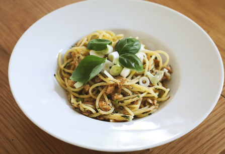 Spaghetti mit Basilikum und Frühlingszwiebeln auf weißem Teller, Holztisch.